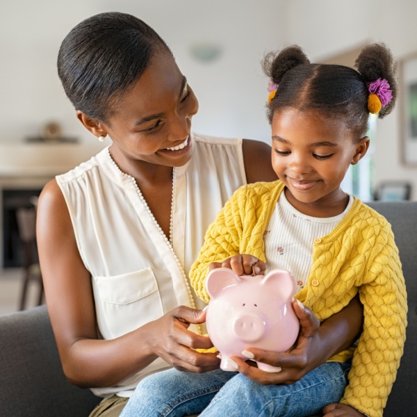 A woman with her child on her knee holding a piggy bank.